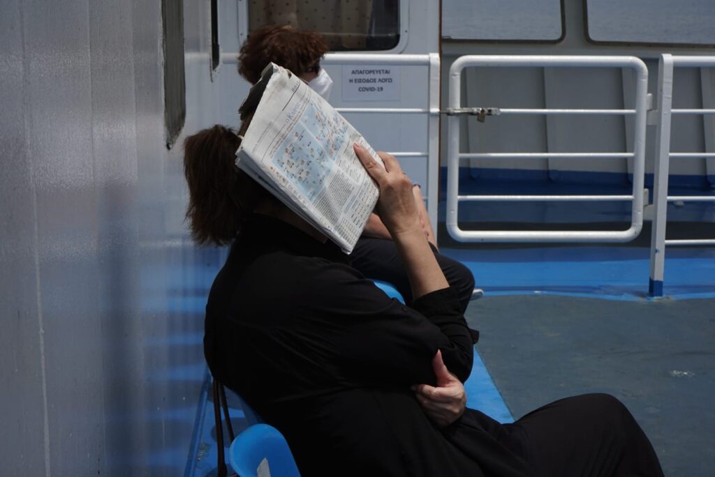 A woman traveler covering head with newspaper for weather forecast to protect herself from the sun.
Αegean sea, June 23,2021.